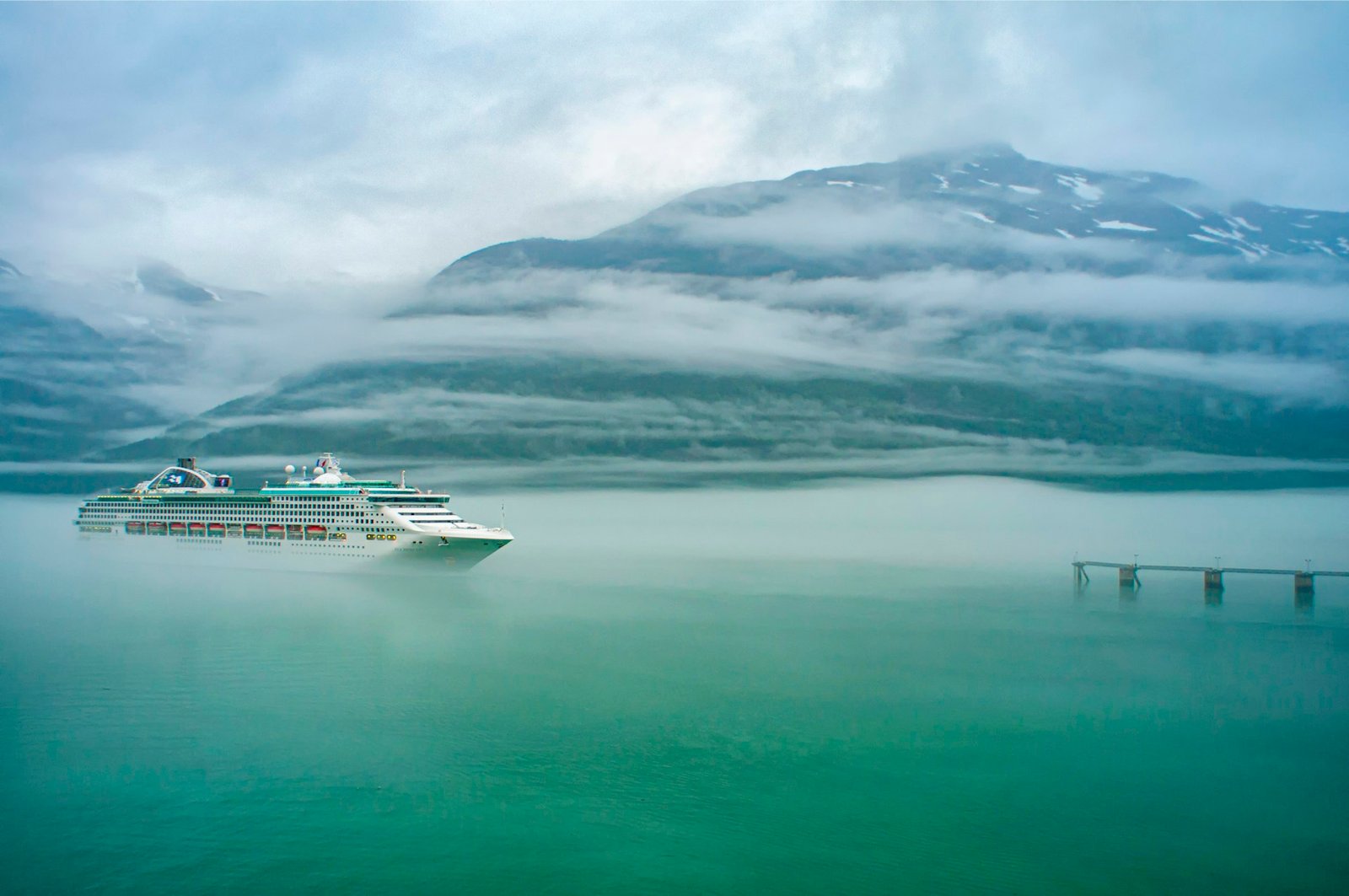 Crucero navegando por un fiordo de Alaska con montañas y niebla al fondo