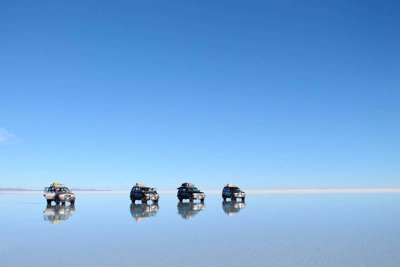 Vehículos sobre el efecto espejo del Salar de Uyuni al atardecer
